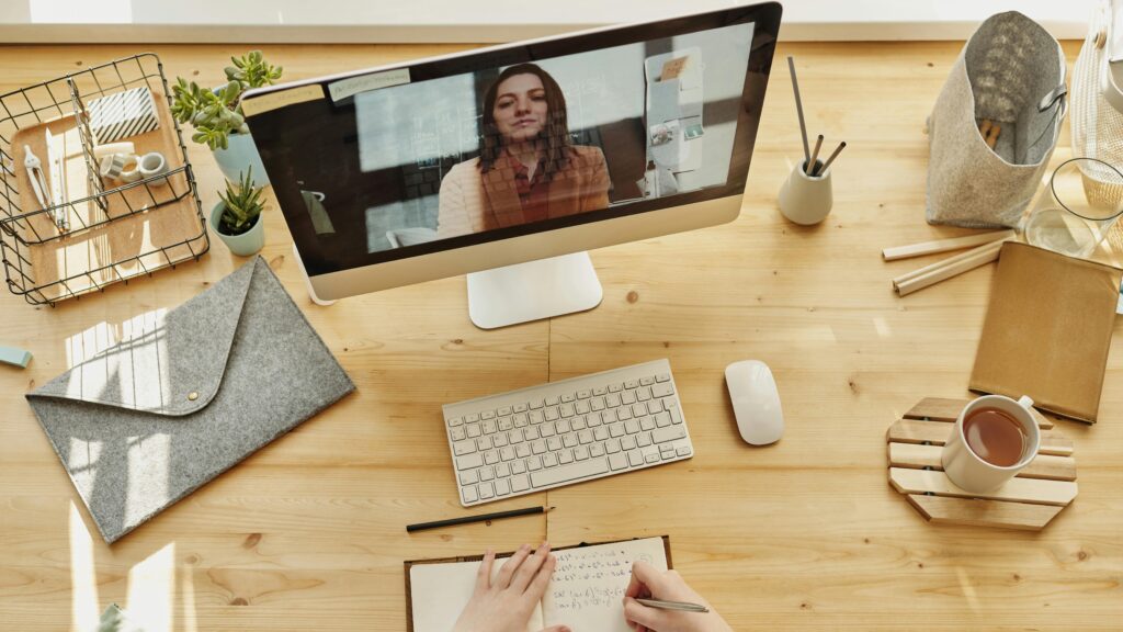Person taking notes during a video call at a neatly organized home desk, showing remote work lifestyle.